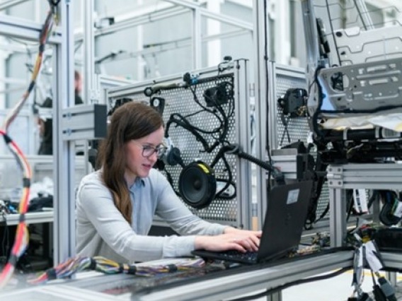 Woman working on a laptop surrounded by machinery and equipment