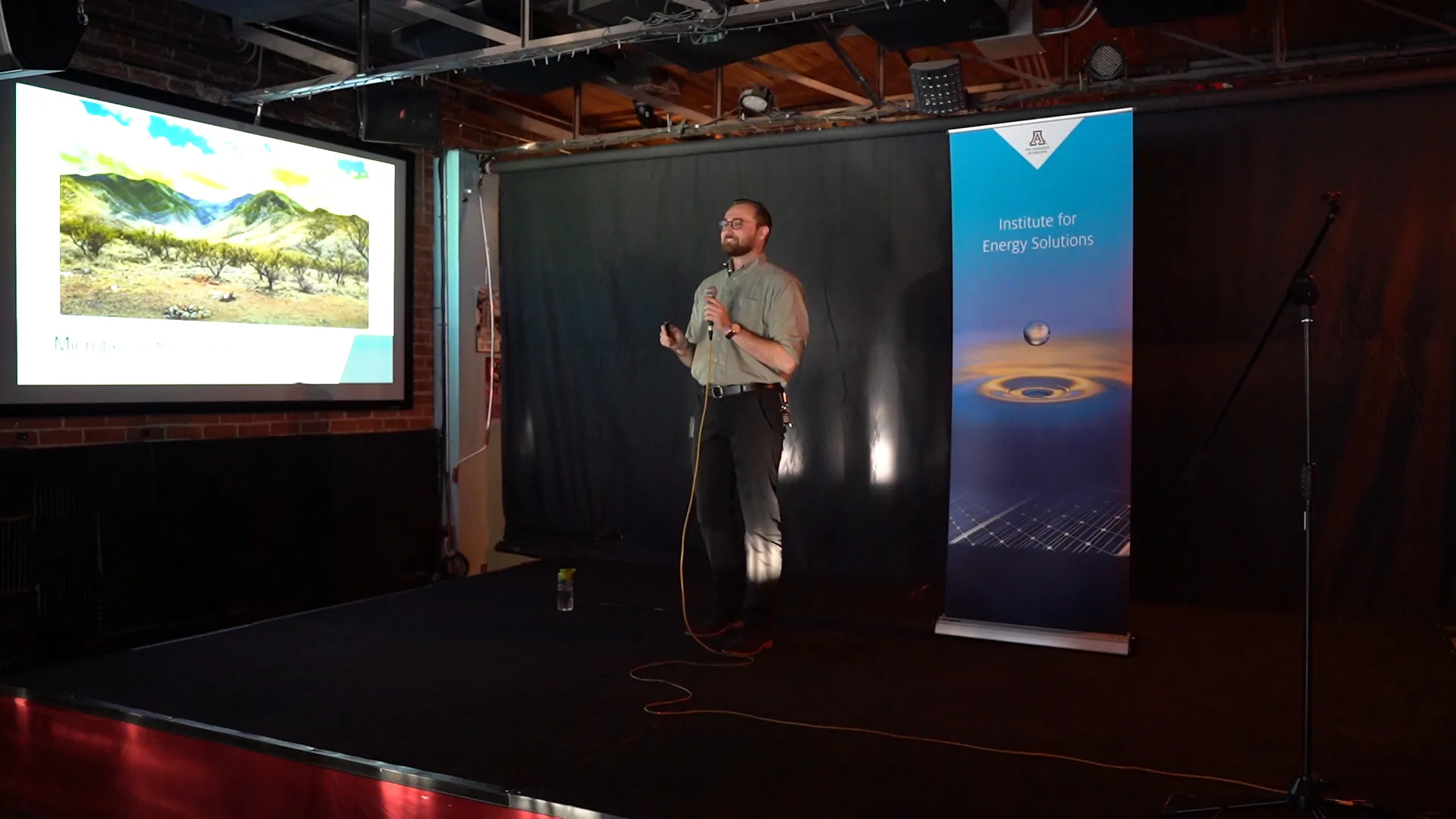 Ashton Leo giving an Energy Talk from a stage with a presentation projected next to him