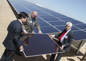 Three men in business suits lifting a solar panel onto the larger collection of solar panels together.