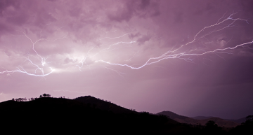 Silhouette of a mountain against a purple sky lit by lighting from a storm